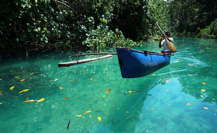Vanuatu tours at Riri Blue Hole, with a person paddling a canoe across crystal clear turquoise water surrounded by lush rainforest